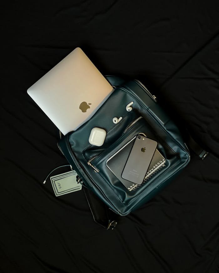 Top view of a backpack with a laptop, smartphone, and earphones, showcasing modern technology essentials.